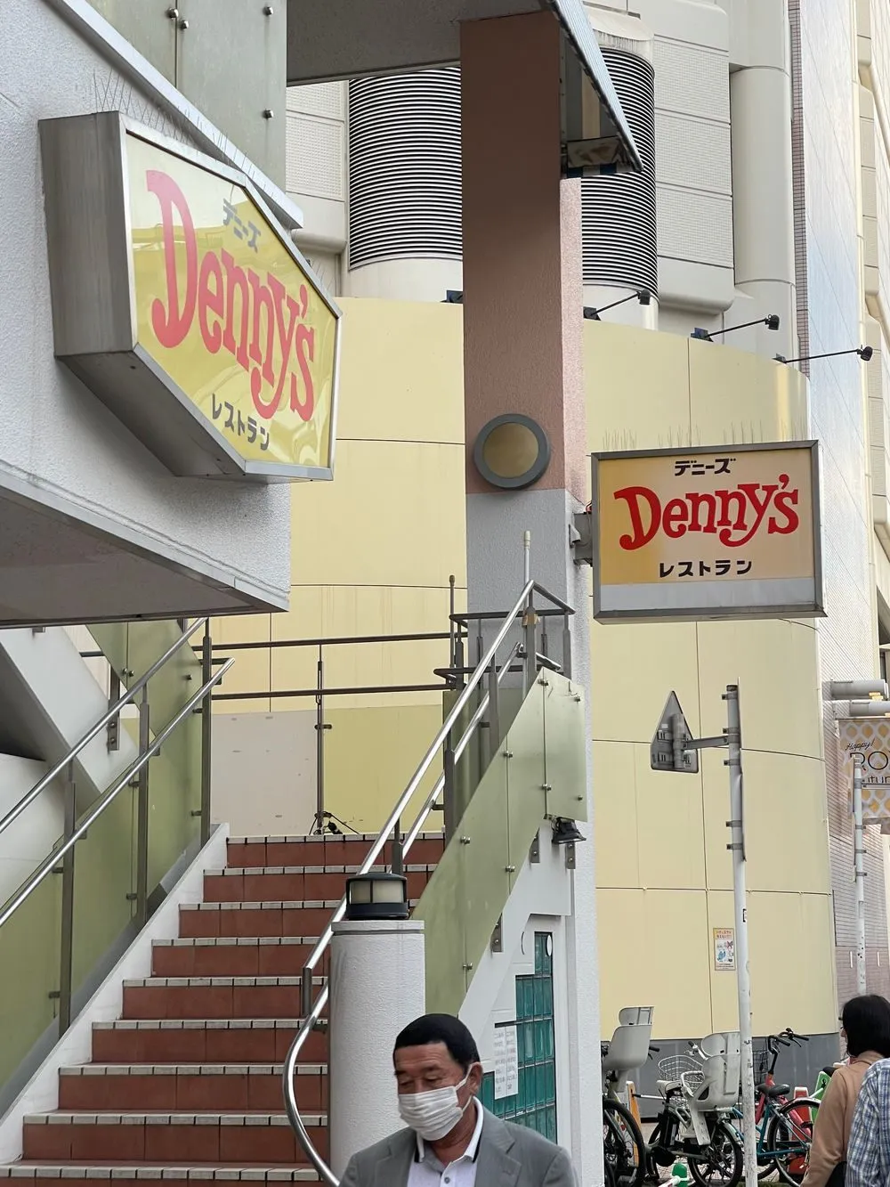 A Denny's restaurant storefront sign in Asakusa, Tokyo, seen from a staircase landing with pedestrians passing below.