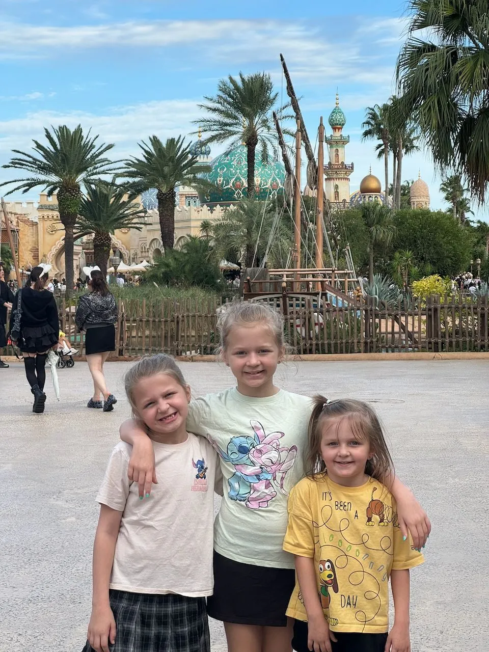 Three young girls stand in front of the ornate domed architecture and palm trees of the Arabian Coast area at Tokyo DisneySea.