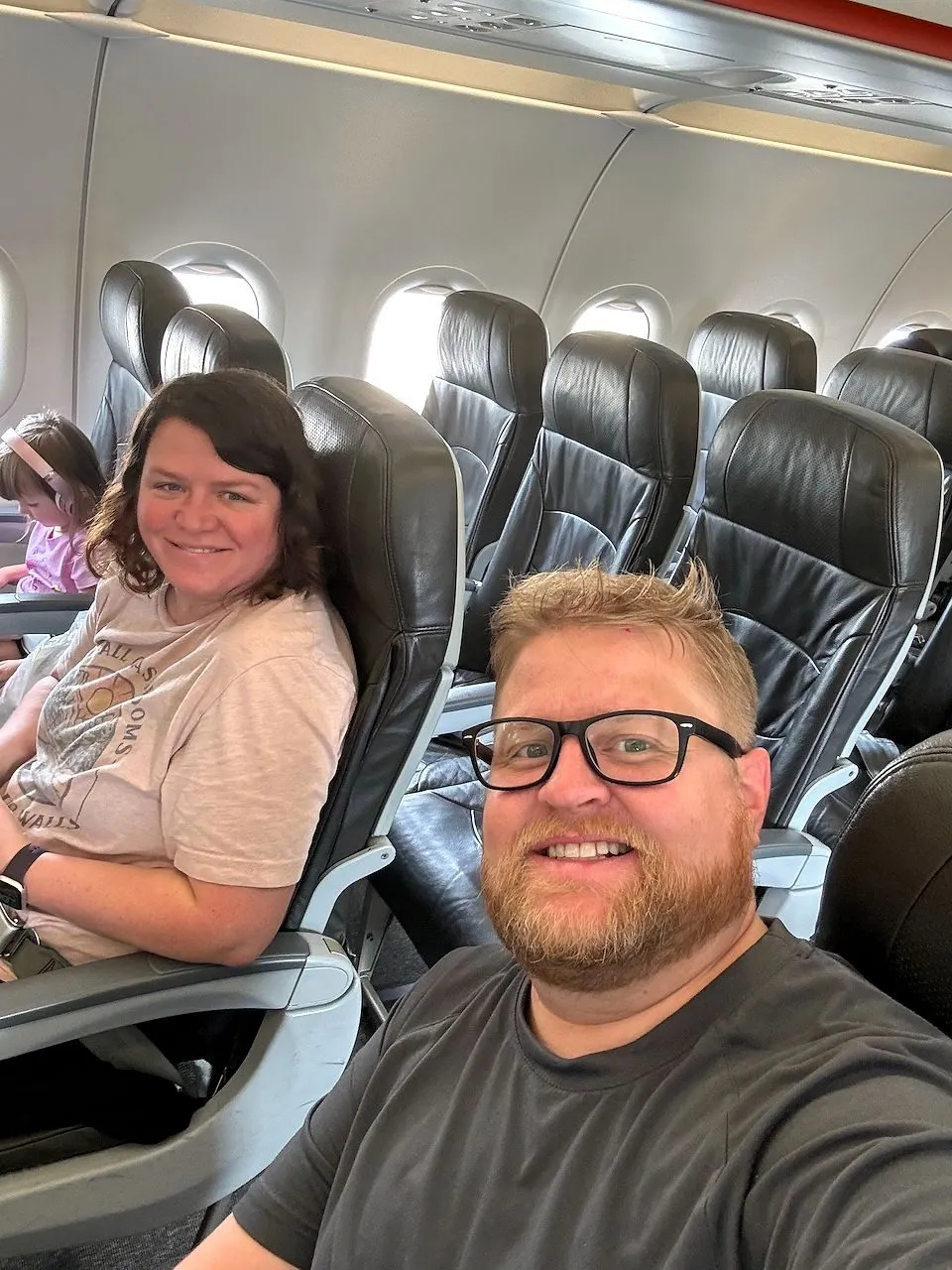 Adam takes a selfie from his airplane seat with Lindsay smiling from the row behind him on a nearly empty flight out of Tokyo.