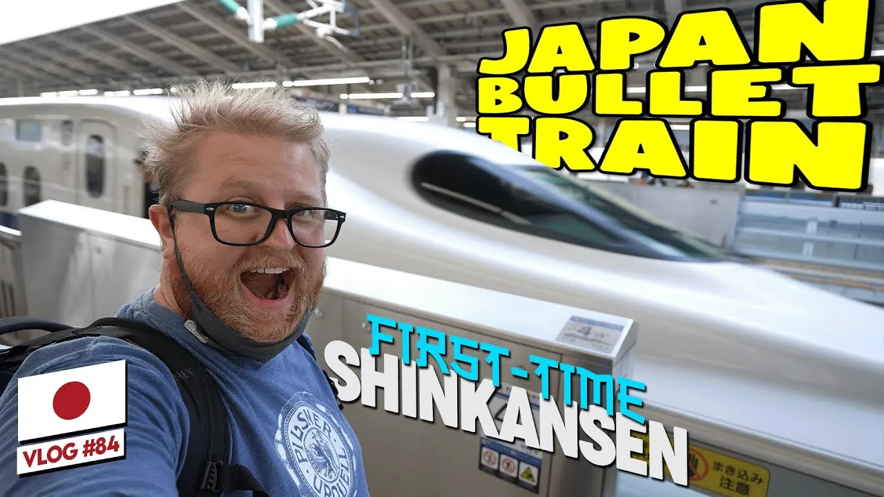 A YouTube thumbnail of Adam Clarkson excitedly posing next to a white and blue Shinkansen bullet train at a Japanese station platform, text reading 'Japan Bullet Train, First-Time Shinkansen.'