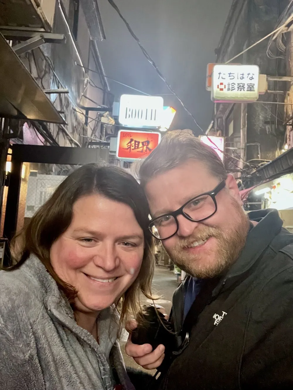 A narrow Tokyo alley at night lined with small illuminated bar signs and lanterns in Shinjuku's Golden Gai district.