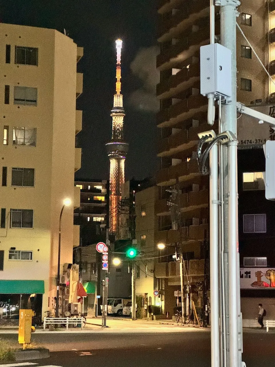 Tokyo Skytree glows orange at the end of a quiet side street in Taito, framed between low-rise apartment buildings at night.