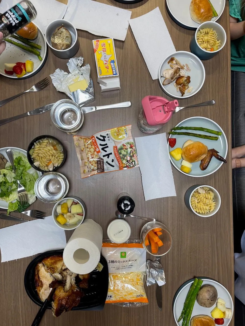 A spread of Thanksgiving food on a Tokyo apartment table seen from above, including roast chicken, baked potatoes, asparagus, pasta salad, and fruit salad.