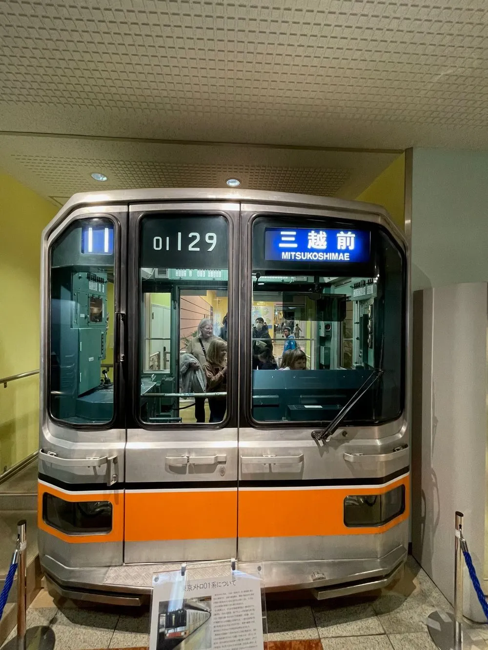 A vintage orange and silver Tokyo Metro subway car on display, front nose visible with a destination sign reading Mitsukoshimae.