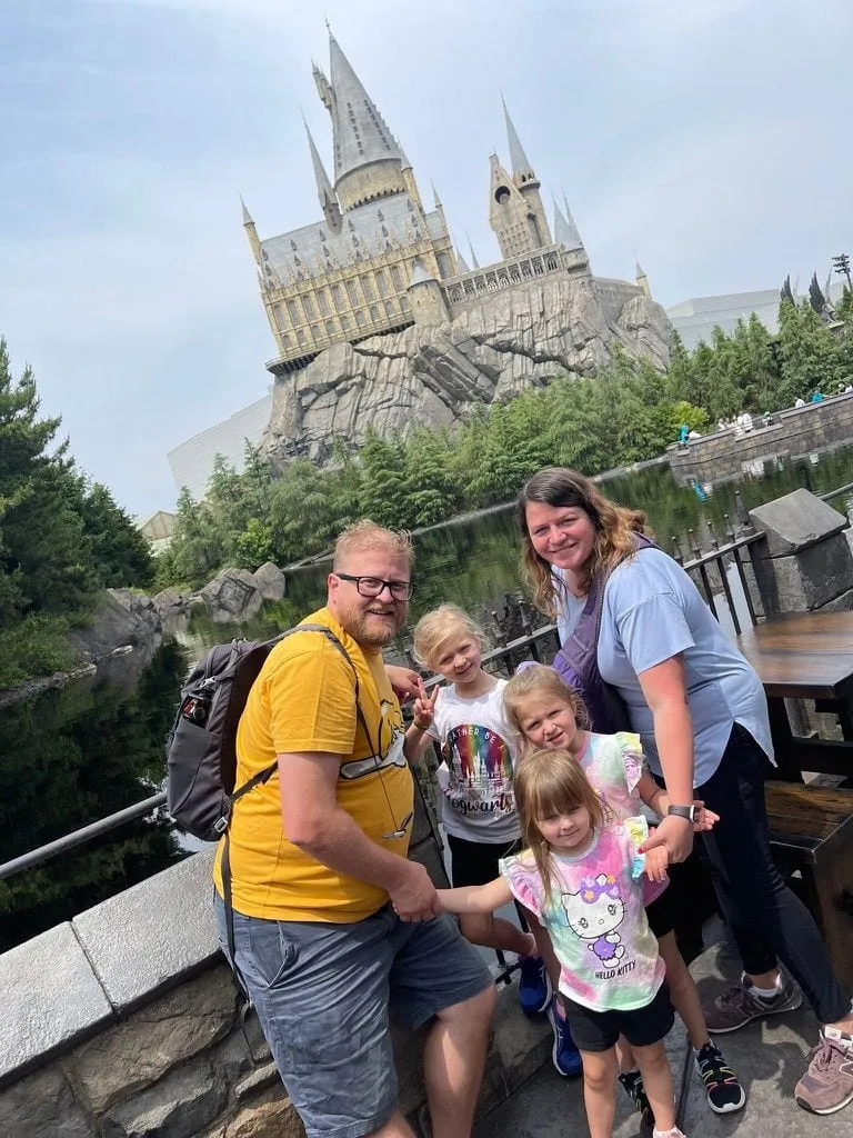 A family of five poses in front of the Hogwarts Castle replica at Universal Studios Japan, with three young girls between the two parents.